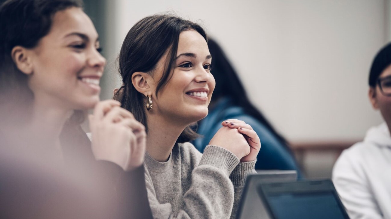 To studenter som sitter og smiler i et klasserom