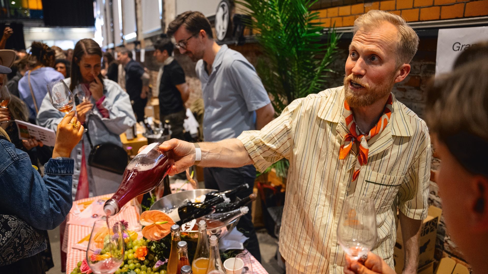 Mann som står og fyller på smaksprøve av naturvin til en gjest på naturvinmesse.