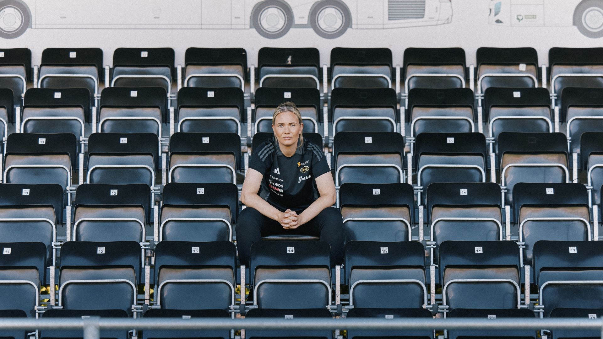 Ung kvinne som sitter på en tom tribune på en fotballstadion.