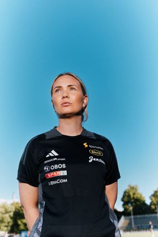 Kvinne i fotballdrakt som ser utover og forbi kamera. 