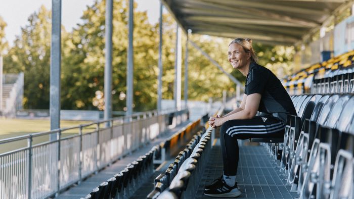 Kvinne som sitter alene på en tribune på fotballstadion.