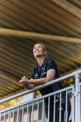 Kvinne i fotballdrakt som står og ser utover en fotballbane.